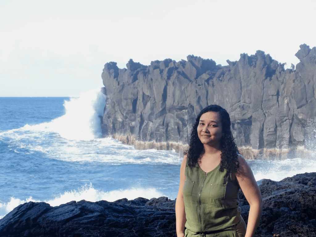 Luz Renaes posant devant une mer agitée dont les vagues se brisent contre les rochers.